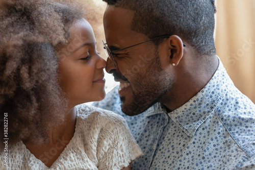 Close up head shot adorable small biracial preschool kid daughter touching noses with affectionate caring young father. Happy peaceful african american family enjoying tender lovely moment at home.