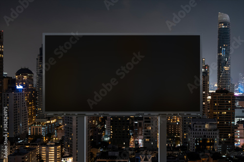 Blank black road billboard with Bangkok cityscape background at night time. Street advertising poster  mock up  3D rendering. Front view. The concept of marketing communication to sell idea.