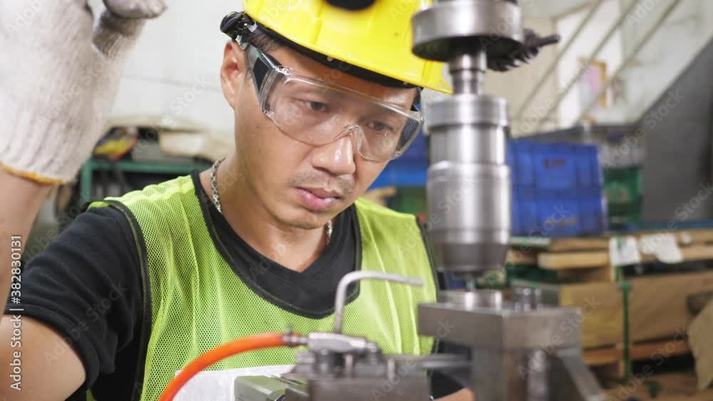 Close up focusing Asian worker operate drilling machine working wear safety glasses uniform and helmet in manufacturing metal sheet factory production line. Dolly camera side view from machine Close up focusing Asian worker operate drilling machine working wear safety glasses uniform and helmet in manufacturing metal sheet factory production line. Dolly camera side view from machine