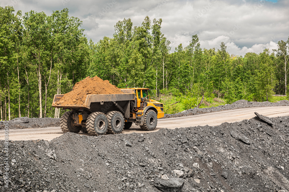 Obraz premium Large quarry dump truck. Big yellow mining truck at work site. Loading coal into body truck. Production useful minerals. Mining truck mining machinery to transport coal from open-pit production