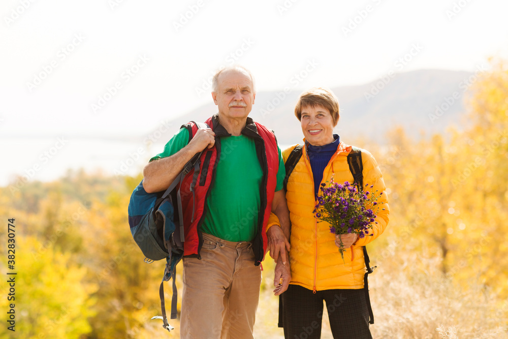 Senior couple  with backpack on a walk in an autumn nature. hyper-local travel,  family outing, getaway, natural environment
