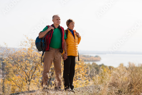 Senior couple  with backpack on a walk in an autumn nature. hyper-local travel,  family outing, getaway, natural environment
