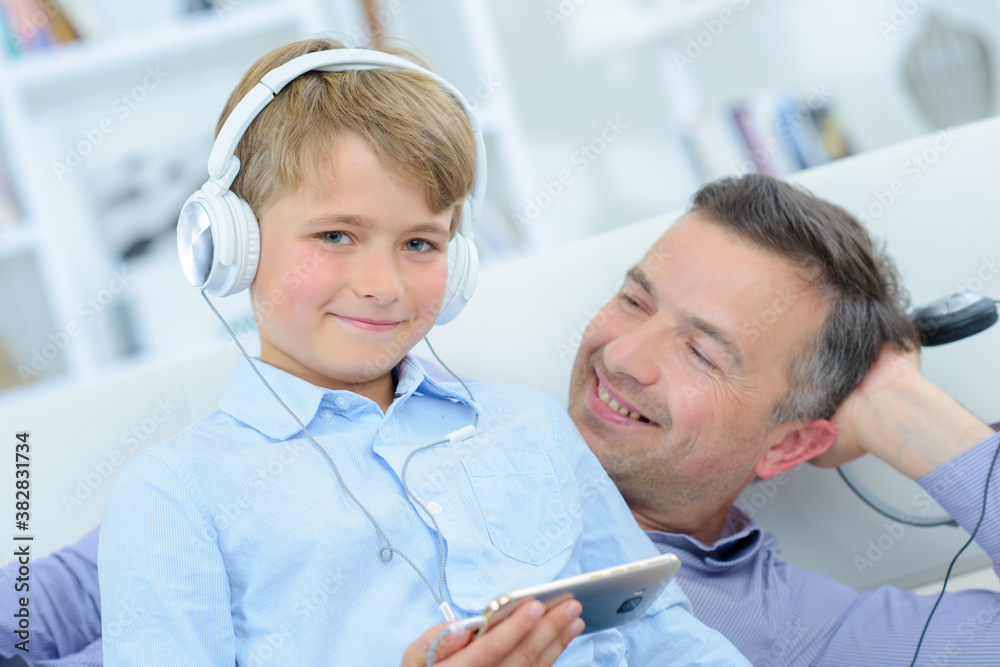 Father and child relaxing on couch wearing headphones Father and child relaxing on couch wearing headphones