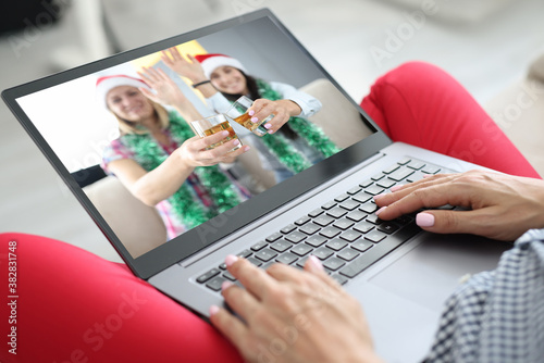 Woman holds laptop on her lap and communicates in messenger in her friends with santa claus hats and protective masks. Christmas and new year during covid 19 pandemic concept.