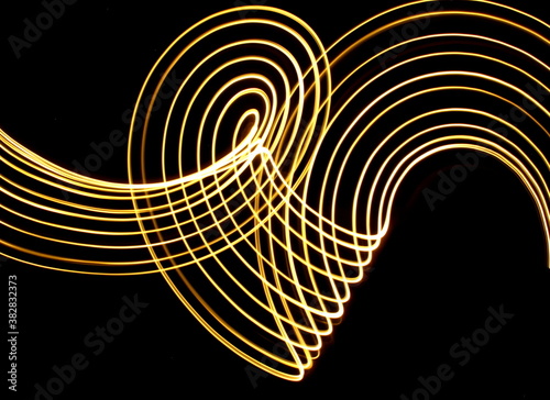 Long exposure photograph of neon gold colour in an abstract swirl, parallel lines pattern against a black background. Light painting photography.