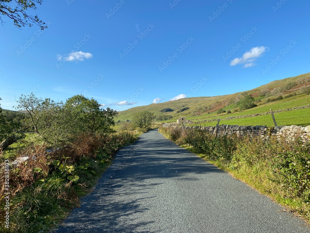 Fototapeta premium Country road, near Halton Gill, with a farm building, dry stone walls, and hills in the distance 