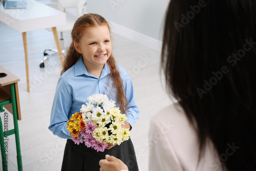 Schoolgirl with bouquet congratulating her pedagogue in classroom. Teacher's day