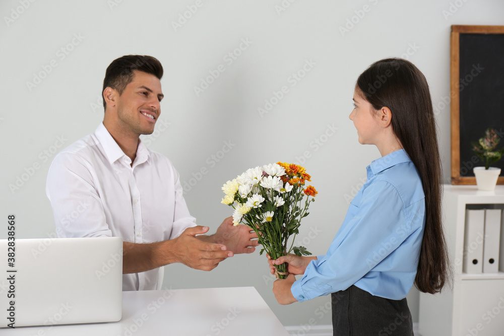 Schoolgirl congratulating her pedagogue with bouquet in classroom. Teacher's day Schoolgirl congratulating her pedagogue with bouquet in classroom. Teacher's day