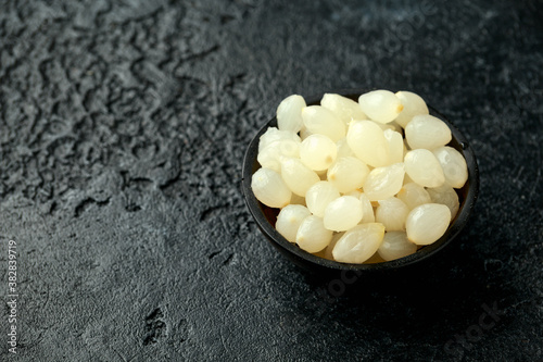 Pickled Cocktail Onions in wooden bowl on rustic black background