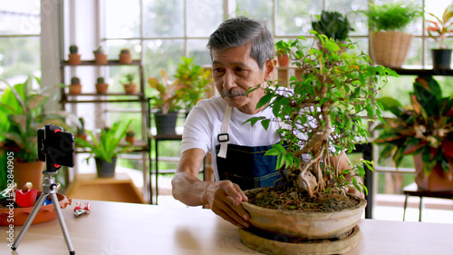 Senior gardener man selling beautiful plants on social media by streaming live from his shop..