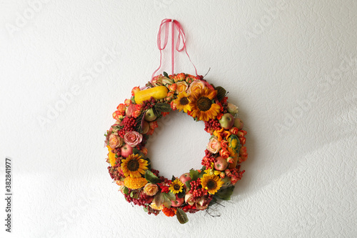 Fototapeta Naklejka Na Ścianę i Meble -  Beautiful autumnal wreath with flowers, berries and fruits hanging on white wall. Space for text