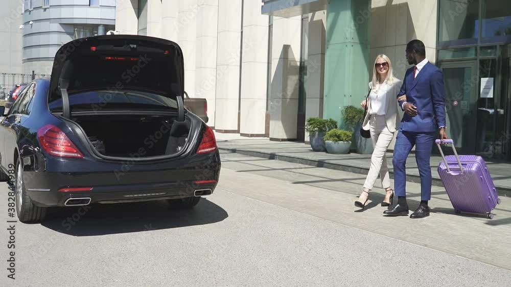 Multiethnic couple leave hotel together, young man and woman in formal wear heading to the car. Multiethnic couple leave hotel together, young man and woman in formal wear heading to the car.