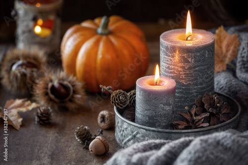 Autumn concept or Thanksgiving celebration concept with two lit candles, orange pumpkin at the background, chestnuts and pine cones photo