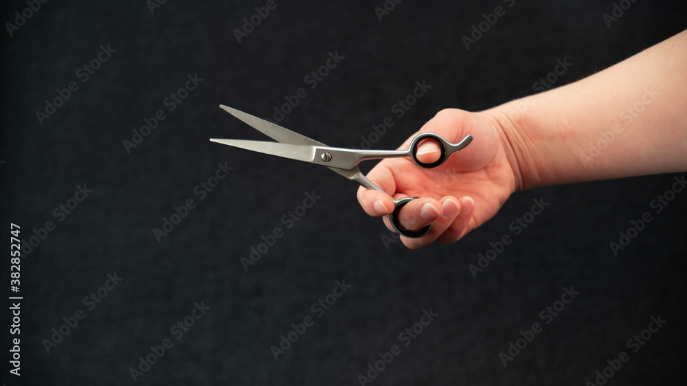 Obraz premium Close-up of a hand holding a pair of hairdressing scissors, on a black background 
