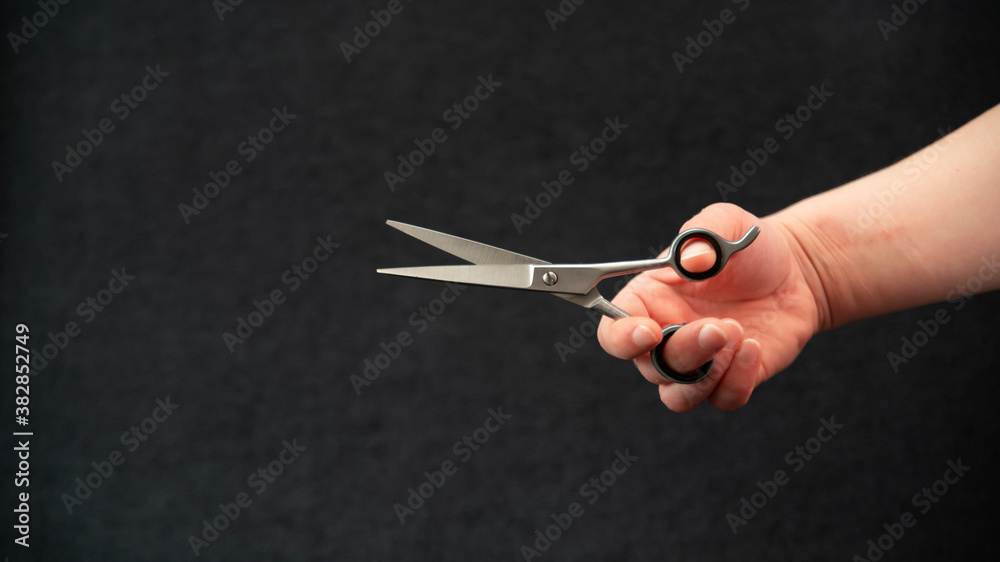 Obraz premium Close-up of a hand holding a pair of hairdressing scissors, on a black background
