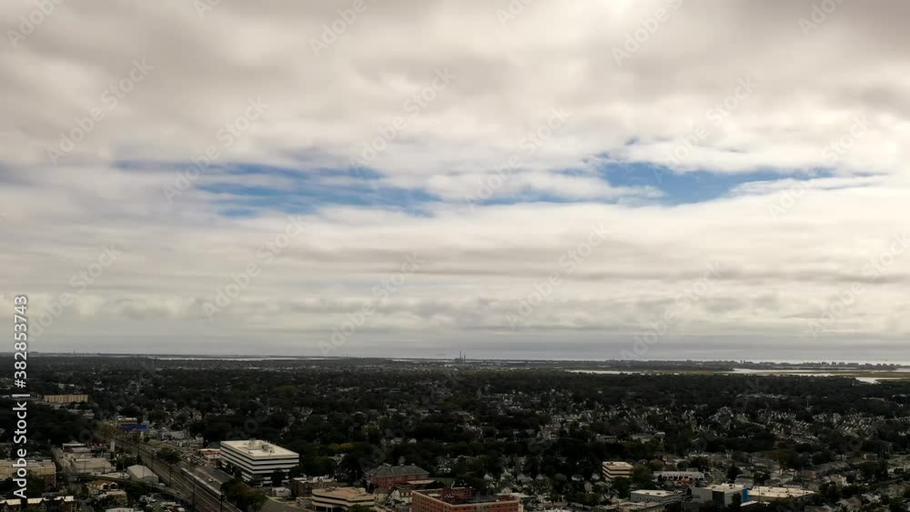 An aerial view over a suburban neighborhood with train tracks and some commercial buildings below. It is a cloudy day with small patches of blue in the sky. The drone is high enough to see the horizon An aerial view over a suburban neighborhood with train tracks and some commercial buildings below. It is a cloudy day with small patches of blue in the sky. The drone is high enough to see the horizon