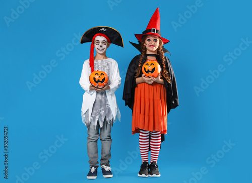 Cute little kids with pumpkin candy buckets wearing Halloween costumes on blue background