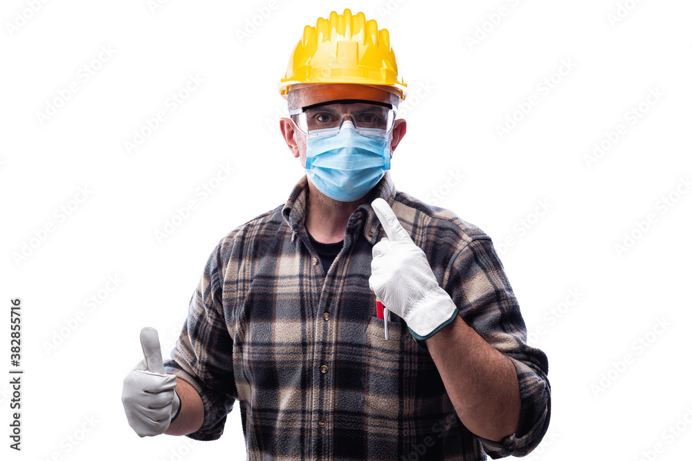Carpenter worker isolated on white background wears surgical mask to prevent Coronavirus spread, makes OK sign with thumb up. Preventing Pandemic Covid-19 at the workplace. Carpenter worker isolated on white background wears surgical mask to prevent Coronavirus spread, makes OK sign with thumb up. Preventing Pandemic Covid-19 at the workplace.