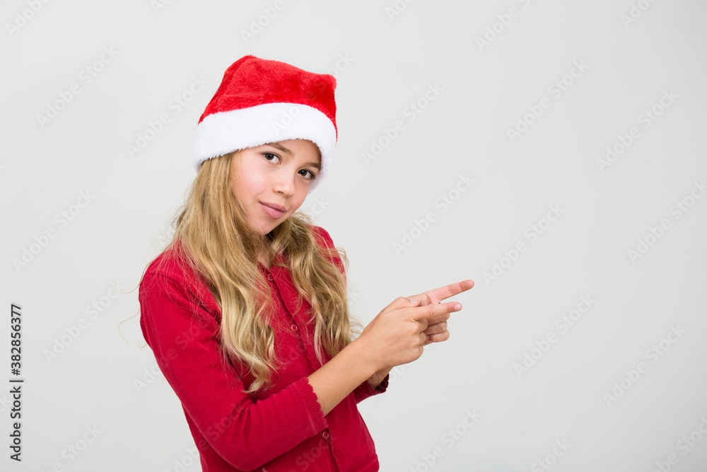 Young smiling, girl in santa hat show with index finger isolated on white background. Kid pointing. Christmas advertising concept,banner copy space.