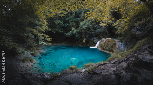 Small waterfall on a turquoise blue lake surrounded by a magical forest in Navarra. Enchanted place with a small turquoise blue lake. Source of the Urederra.  © Quique