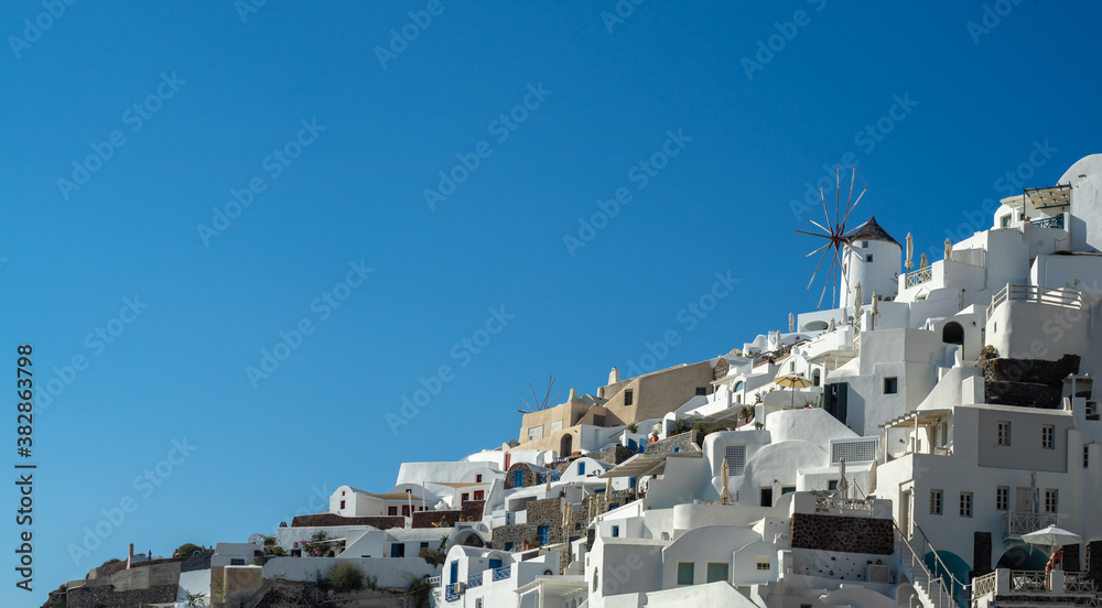 Panoramic view of Oia town in Santorini island with old whitewashed houses and traditional windmill, Greece. Greek landscape on a sunny day
