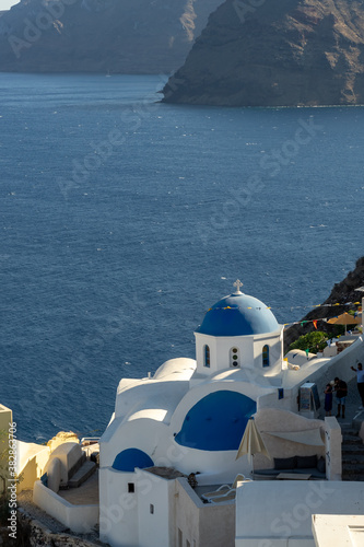 View of Oia, Santorini, with typical blue dome church, caldera, sea and flags