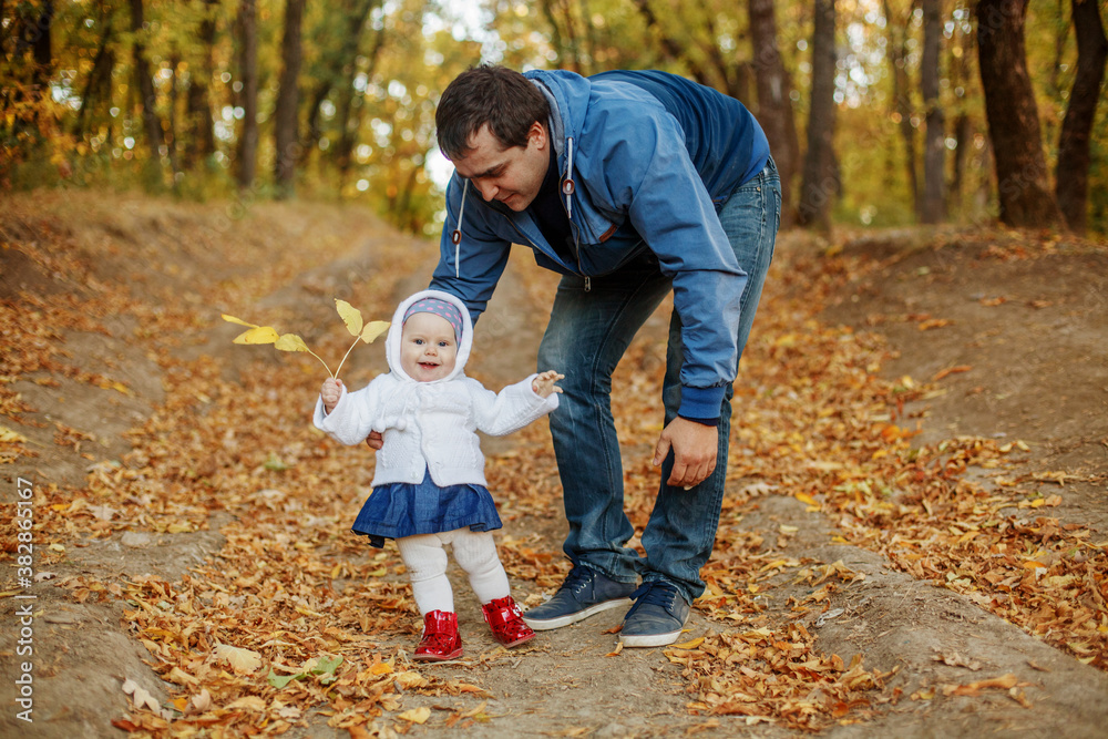 Fototapeta premium Young dad teaches his little daughter to walk in the Park in the fall