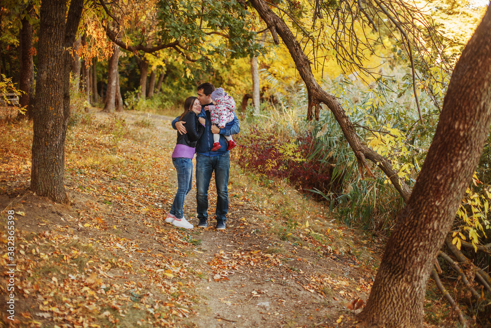 Young parents with a child in their arms walk along the path in the autumn Park Young parents with a child in their arms walk along the path in the autumn Park