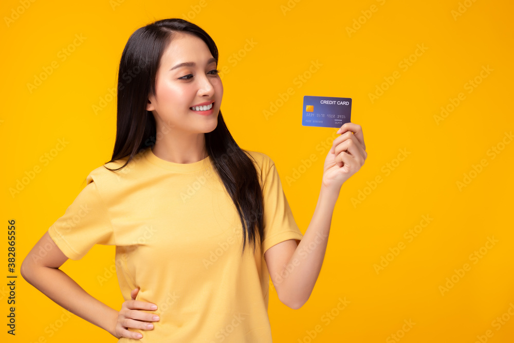 Portrait lovely young asian woman showing plastic credit card and looking at credit card, standing over yellow background. Beautiful girl get satisfied of credit card service with smile on face Portrait lovely young asian woman showing plastic credit card and looking at credit card, standing over yellow background. Beautiful girl get satisfied of credit card service with smile on face
