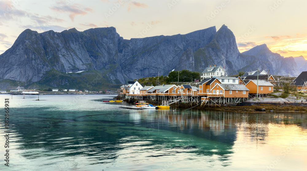 Traditional yellow rorbu house in drying flakes for stockfish cod fish in norwegian fjord in summer. Sakrisoy fishing village, Lofoten islands, Norway