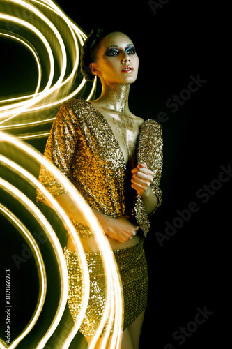 Long exposure portrait. High Fashion model woman with bright golden sparkles on skin posing. Portrait of beautiful girl glowing make-up. Art design gold sequins make up. Glitter glowin photo