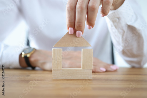 Woman build house from wooden cubes on table. Purchase and construction of residential building. © H_Ko