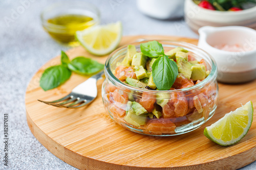 Delicious avocado and raw salmon salad, tartare, served glass jar with lime, light background