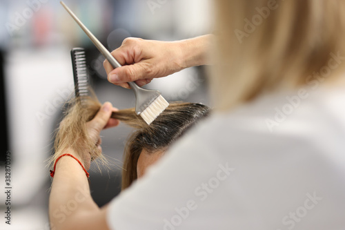 Hair dye with brush close-up. Woman hold lock of client hair and makeover.