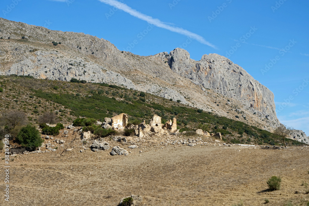 Ruins of a farm house at the bottom of an impressive rock formation with blue sky near Alhama de Granada in Andalusia, Spain, Europe