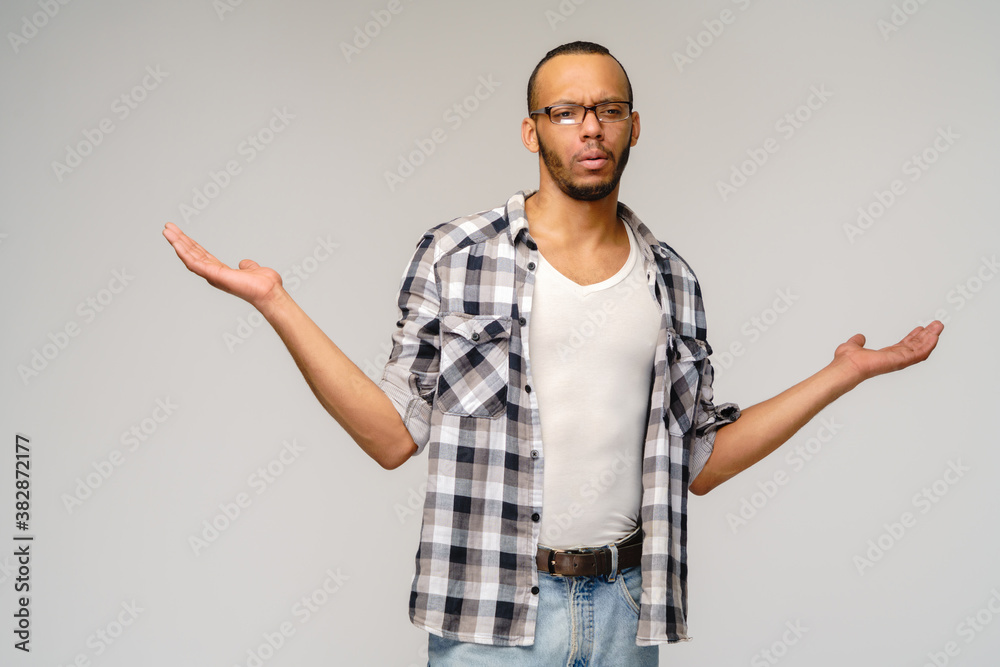 I don't know gesture - Young afrcian american man over grey background being at a loss, showing helpless gesture with arm and hands, as if he does not know what to do I don't know gesture - Young afrcian american man over grey background being at a loss, showing helpless gesture with arm and hands, as if he does not know what to do
