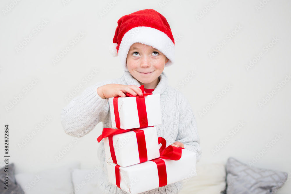Excited smiling little boy in red santa hat with gift many boxes isolated on white background, banner copy space. Christmas congratulation concept. Excited smiling little boy in red santa hat with gift many boxes isolated on white background, banner copy space. Christmas congratulation concept.