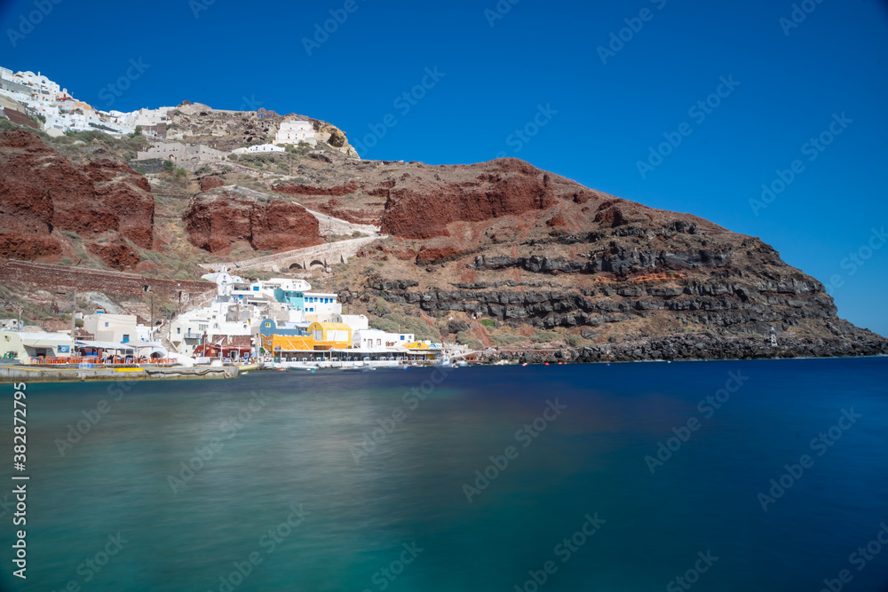 Beautiful panoramic view from the old harbor of Ammoudi under the famous village of Oia on a sunny day. Picturesque natural background. Santorini island, Cyclades, Greece, Europe.