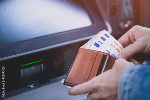 Принти на полотні Unrecognizable man putting euro bills withdrawn from the ATM in his pocket walle