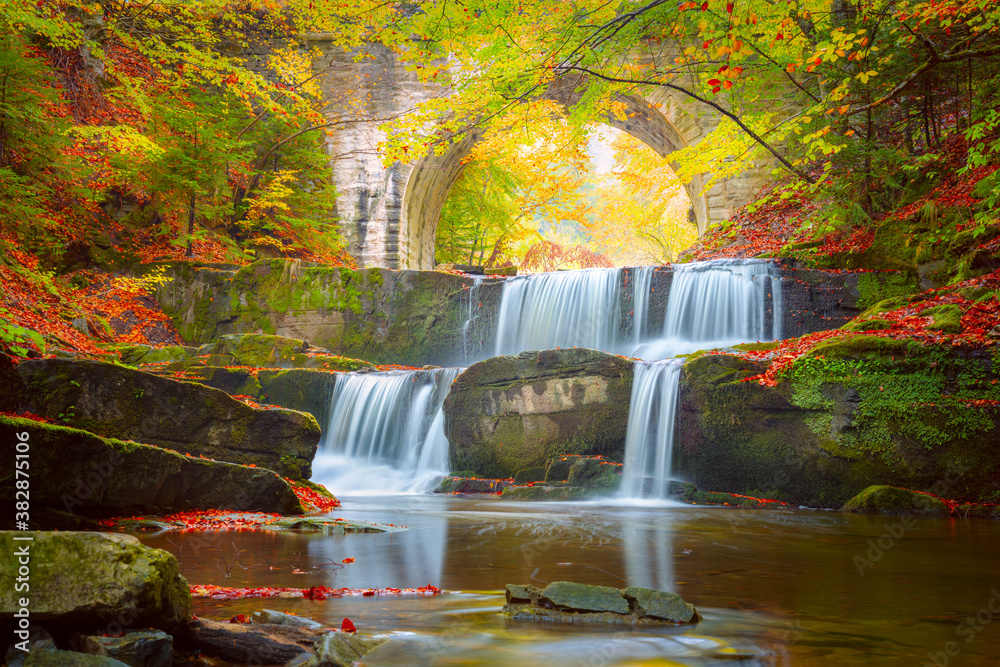 Fototapeta premium Autumn natural landscape - river waterfall in colorful autumn forest with old bridge