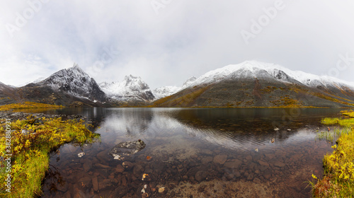 Panoramic View of Beautiful Alpine Lake surrounded by Snowy Mountains in Canadian Nature. Season change from Fall to Winter. Taken at Grizzly Lake in Tombstone Territorial Park, Yukon, Canada.