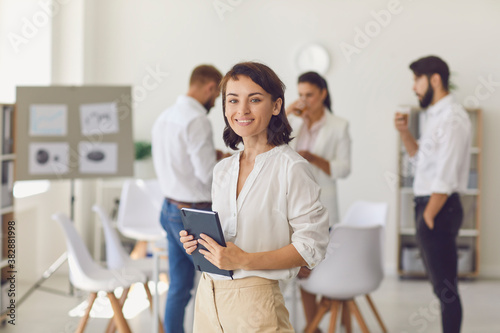 Happy successful businesswoman or company leader standing in office looking at camera and smiling