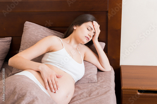 Young pretty pregnant woman suffering from headache at home in bed