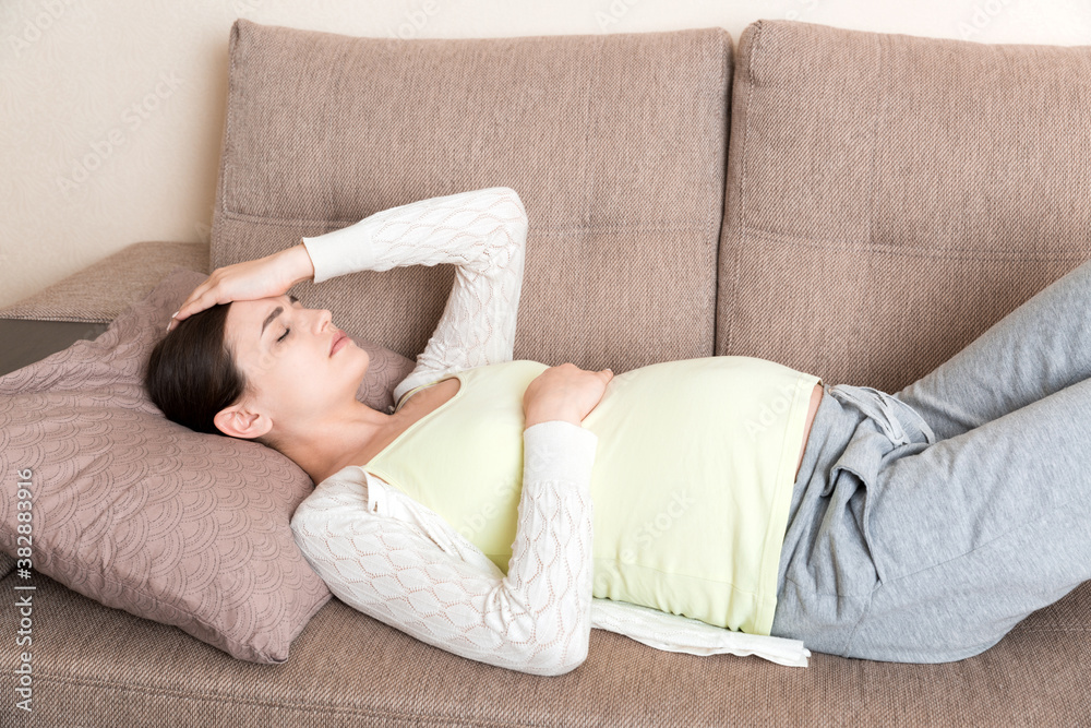 Pregnant woman with painful belly on sofa at home