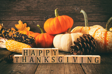 Happy Thanksgiving greeting on wooden blocks against a rustic wood background with pumpkins and autumn decor. Vintage style.