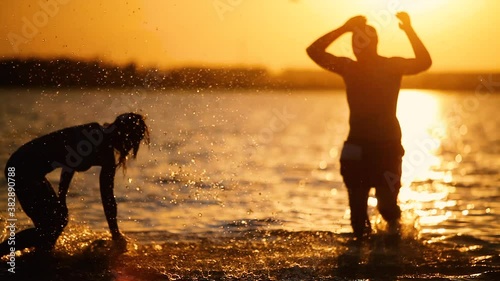 Young people in swimsuits spray splash on beach at sunset in summer ocean sea. Tourists having fun sunny splashing. Friendship freedom travel vacation holidays, girl and guy happy family 