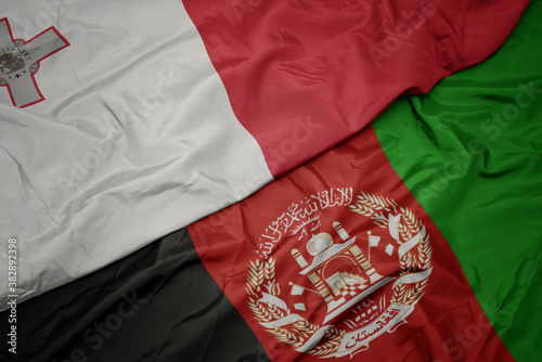 waving colorful flag of afghanistan and national flag of malta. macro