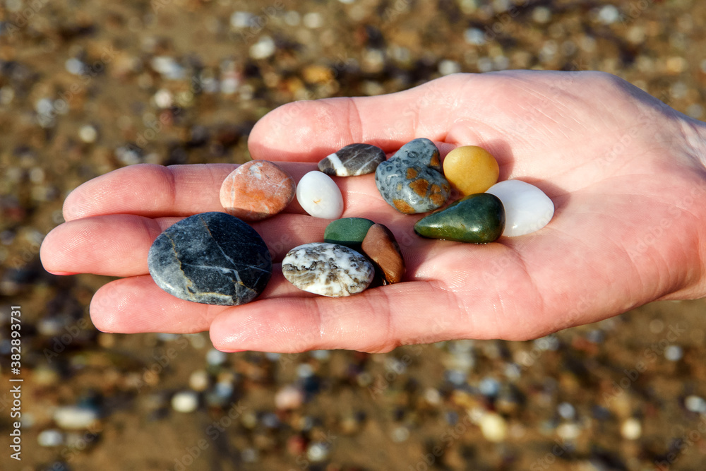 close-up of female hands holding colorful beach rocks with blurred beach background. close-up of female hands holding colorful beach rocks with blurred beach background.