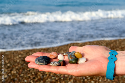close-up of female hands holding colorful beach rocks with blurred beach background.