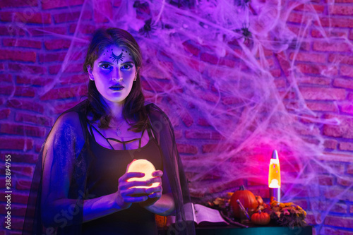 HHalloween witch, young woman disguised as wicca holding a magic ball over spiderweb background with altar
 photo